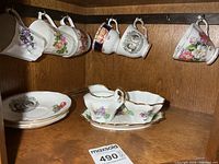 All items arranged on shelf: mugs hanging, teacups/saucers stacked, cream & sugar set in centre