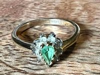 Ring top view showing green center stone, clear halo stones, and band color