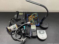 Group shot of all electronics including calculator, lamp, phone, CD player, cables, case