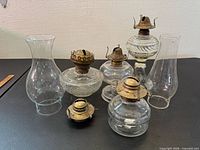 Group of four glass oil lamp bases with burners, two chimneys, one loose burner