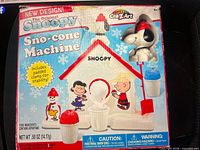Front of box showing Snoopy Sno-cone Machine graphics and accessories