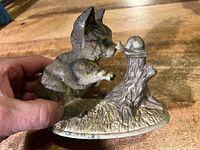 Left side view of ceramic cat reaching toward snail on stump