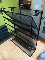 full view of black metal mesh wall file rack showing four pockets and mounting holes
