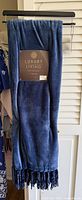 Full view of blue Luxury Living throw blanket hanging, showing fringe and attached tag