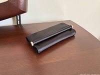 Front three-quarter view of black satin clutch showing gold-tone end caps