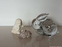 Front view of three rabbit figurines: clear glass, cream/tan ceramic, brown ceramic