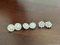 All three pairs of silvertone clip-on earrings displayed side by side on wooden surface