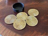 Five textured gold round coasters and black holder displayed on wood surface
