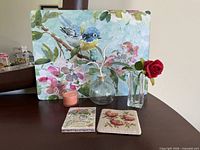 All items displayed: bird art board, glass bottle with owl stopper, bud vase with rose, candle, two coasters