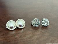 Both pairs of earrings on wood surface: domed pair left, knot pair right