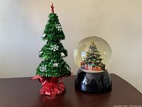 Tinsel tree and snow globe side by side on table