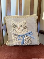 Front view of square pillow showing cat needlepoint design and piping trim