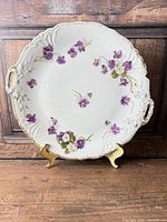 Front view of porcelain plate on stand showing floral decoration, handles and gilt rim
