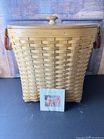 Front view of Longaberger woven wood oval waste basket with lid, leather handles, plastic protector and booklet