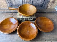 Four honey-brown wooden bowls on table, one with handle