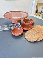 Group shot of all items: terracotta riser, three saucers, four cork coasters, glass block tealight holder