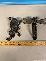 Overall view of frog and dragonfly wall hooks beside ruler for scale