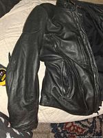 Black leather motorcycle jacket folded on bed showing front zippers and sleeves