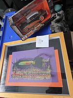 Group shot of boxed Maisto car and framed textile art