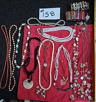 Overview of lot showing all necklaces laid on red cloth and two shell stretch bracelets above