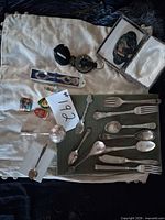 Group shot showing all flatware, compass keychain, boxed items, enamel pins on cloth