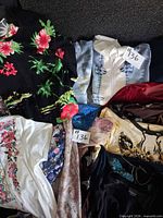 Array of eight tops laid out showing satin blouses and black floral knit sweater