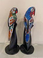Front three-quarter view of both parrot sculptures showing mosaic colours and wooden bases