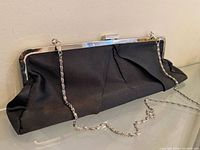 Front view of black pleated satin purse showing silver frame and chain strap