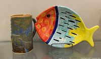Fish-shaped plate standing on display stand beside stoneware mug