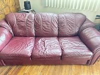 Front view of burgundy leather three-seat sofa showing cushions and armrests