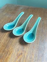 three ceramic turquoise and green Chinese soup spoons on wood surface