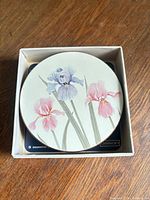 Coaster on top of open box showing iris design and cork backing edge