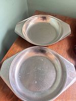 Two stainless steel serving dishes on table top, showing shape, size and handle style