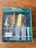 Boxed set showing four stainless steel spreader knives with novelty food handles
