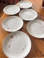 Six white porcelain salad plates on table, floral design visible