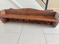 Front view of brown solid wood wall shelf showing seven pegs and top shelf