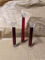 Three glass candle holders standing upright showing red stems and clear tops