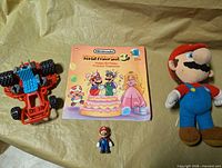 Group shot of all items: book, plush Mario, small Mario figure, red buggy
