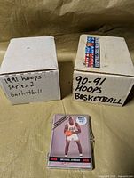 Two white storage boxes marked 1991 Hoops Series 2 and 90-91 Hoops Basketball with plastic-cased USA Basketball set in front