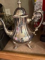 Front and side view of silver plated teapot on shelf