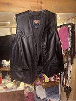 Front view of black leather vest on hanger showing snap closure and pockets