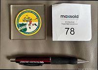 Front view of acrylic block showing embroidered badge, size reference pen and lot card visible