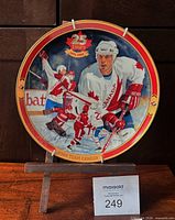 Front view of commemorative plate showing artwork, diameter reference, plate stand