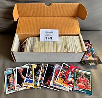 Open cardboard box with full row of basketball cards; sampling of cards including John Stockton, Karl Malone, Clyde Drexler, Hakeem Olajuwon displayed in front