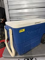 Overall view showing Coleman logo, blue body, cream lid, long pull handle, wheels