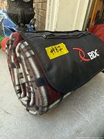 Rolled fleece picnic blanket with BDC-branded flap shown on concrete surface
