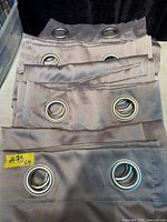 Four grey grommet curtain panels stacked, showing metal ring headers