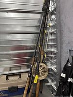 Cluster of assorted vintage fishing rods leaning against wall with visible reels attached