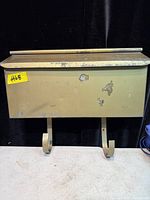Front view of beige metal mailbox showing lid, body, hooks, paint chips