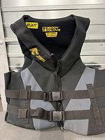 Front view of black and grey Body Glove life jacket showing logo, zipper, and buckle straps